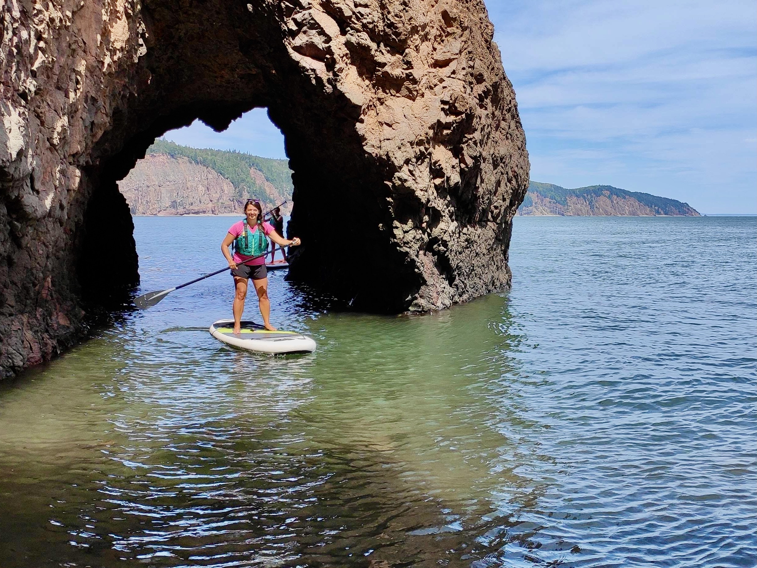 Two paddle boarders paddling through a cliff arch at cape d'Or